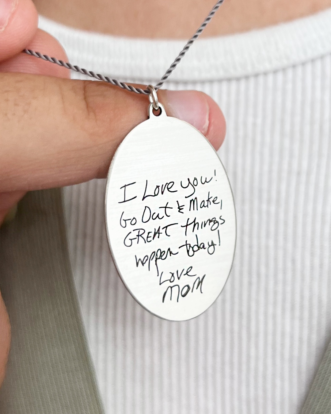 Silver necklace with an oval pendant featuring handwritten text held by a person | Scripted Jewelry