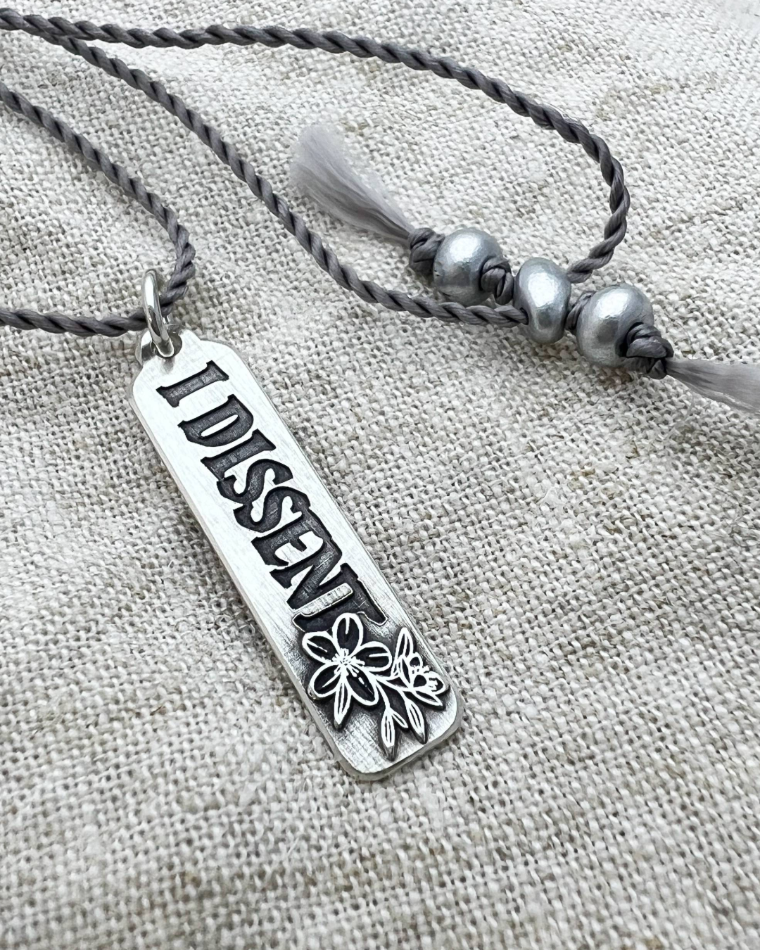 Silver necklace with 'DISSENT' pendant on a textured fabric background