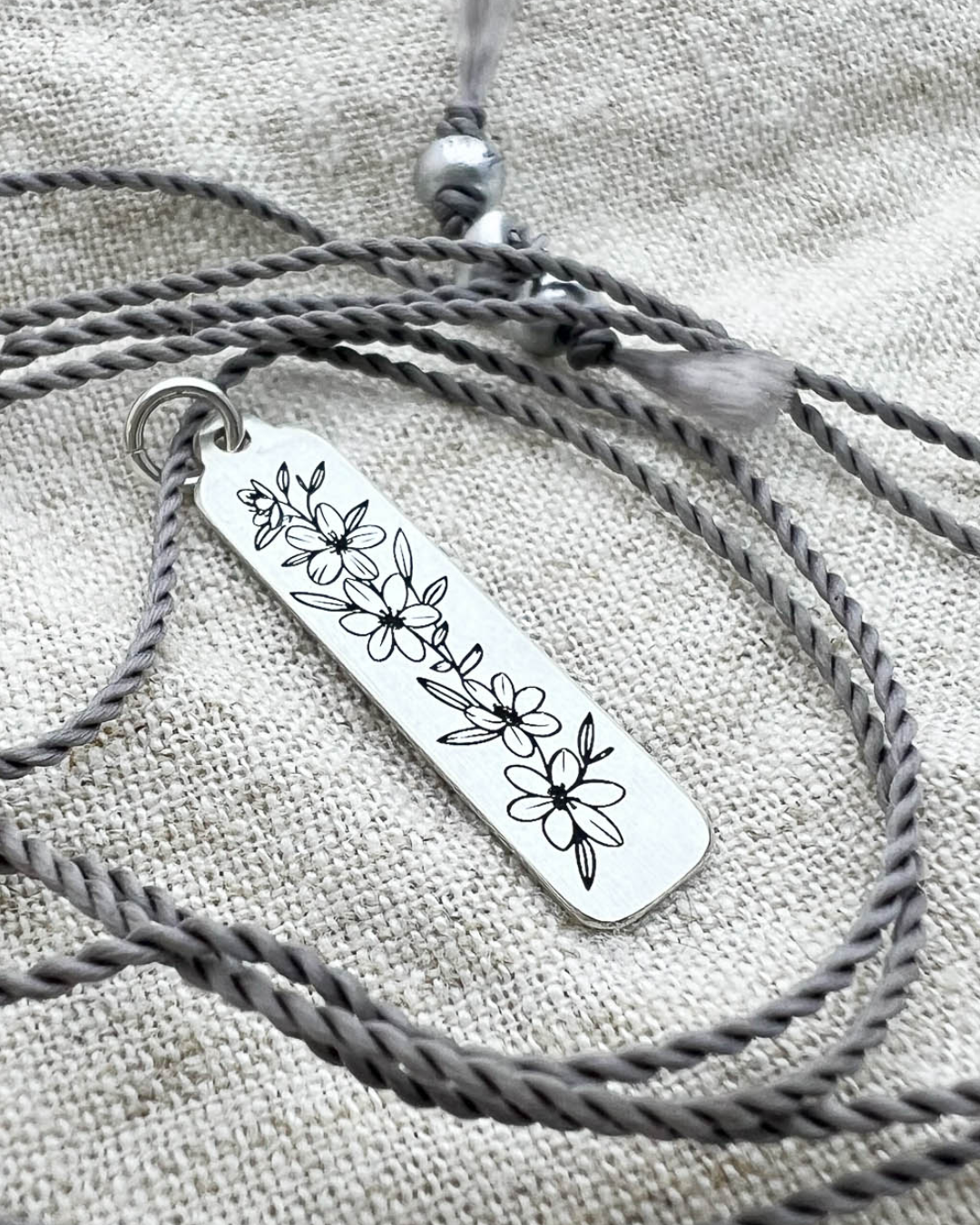 Silver necklace with a floral pendant on a textured fabric background