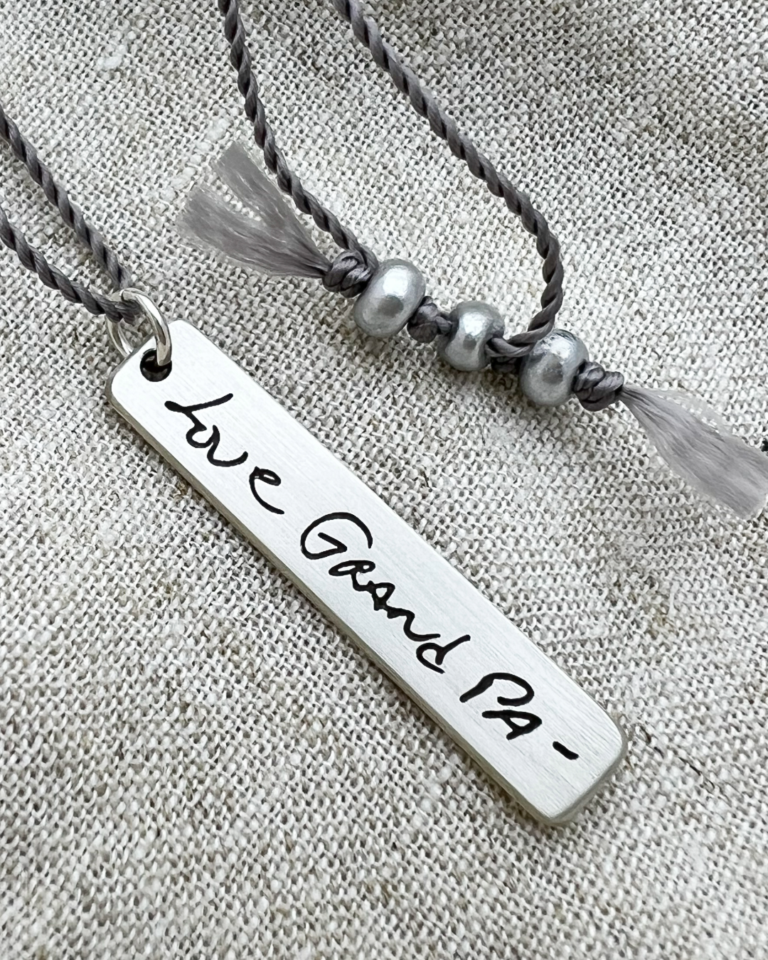 Necklace with a bar pendant engraved with 'Love Grand Pa' handwriting on a textured fabric background - Scripted Jewelry