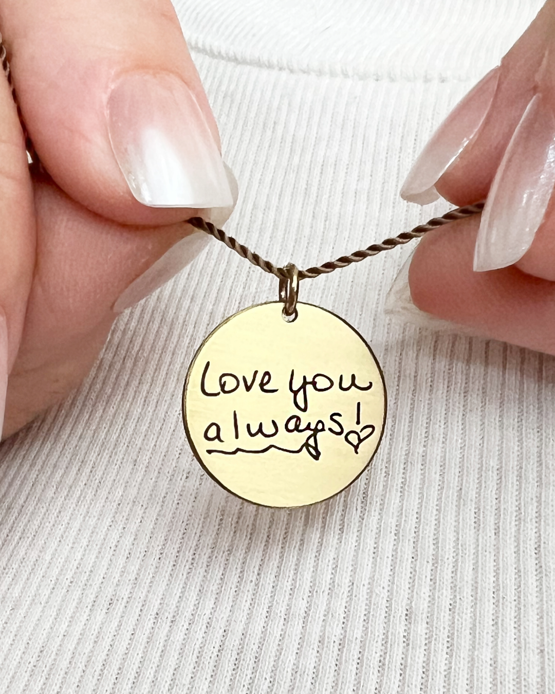 Gold necklace with 'Love you always!' pendant held by hands on a light background