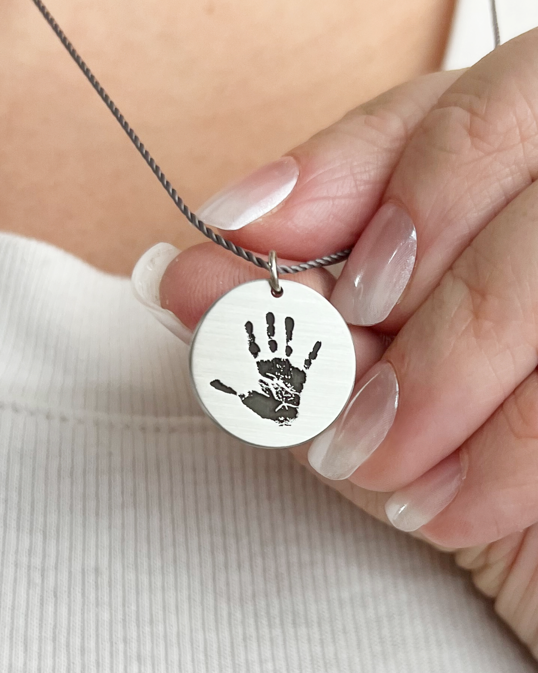Round silver pendant engraved with handprint being held in hand.