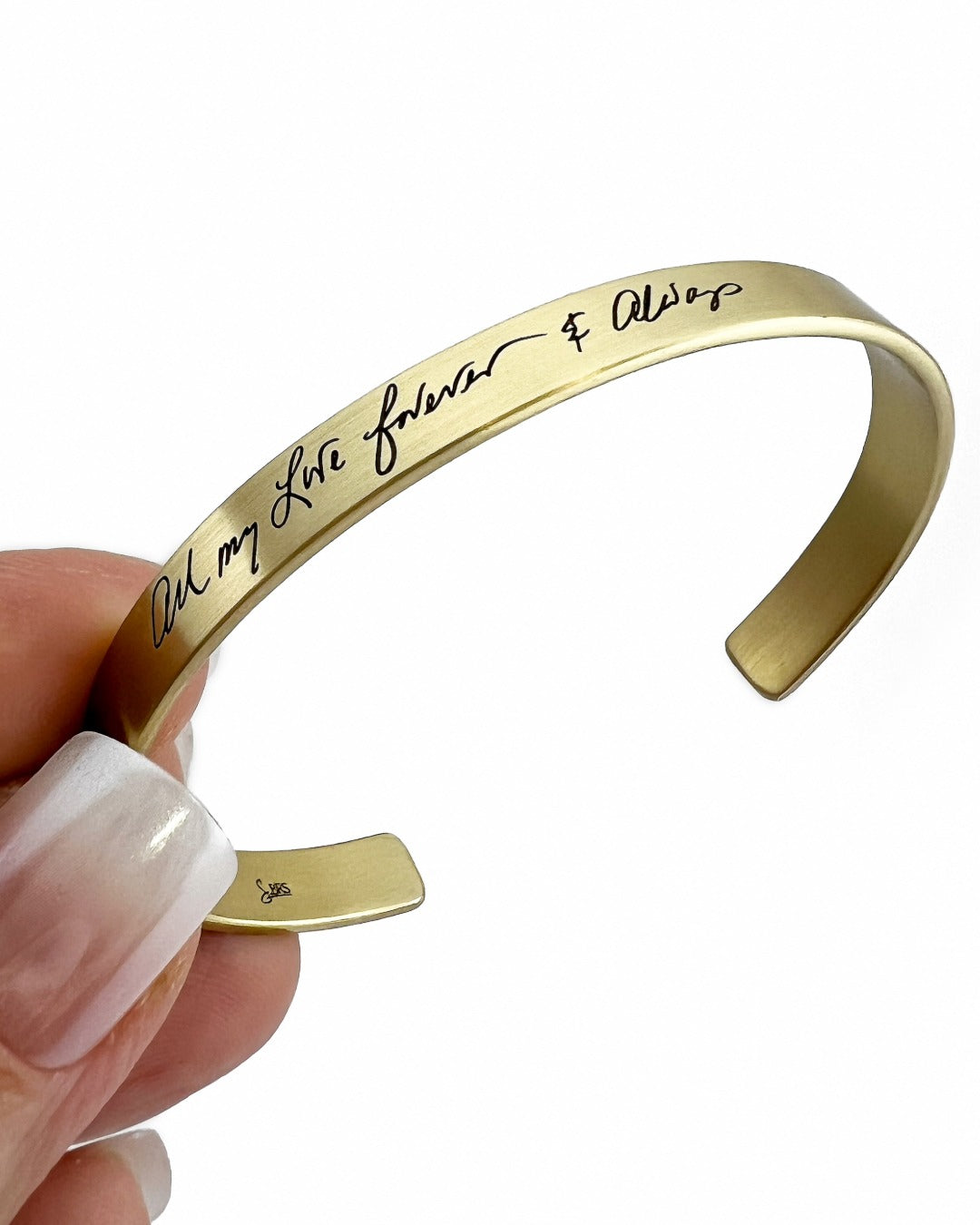 Brass bracelet with engraved text held by a hand on a white background