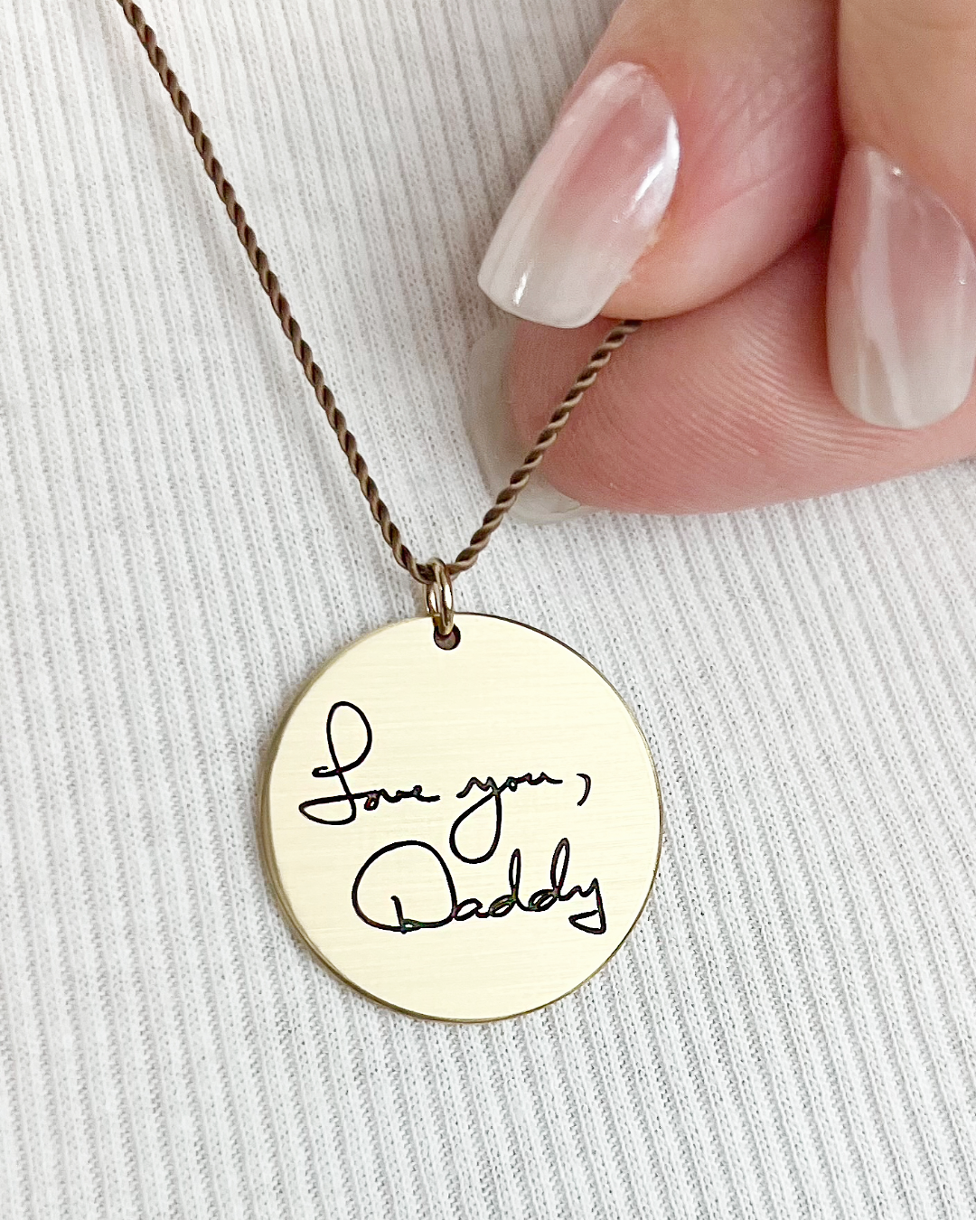 Golden brass round necklace with 'Love you, Daddy' pendant held by a hand on a light background