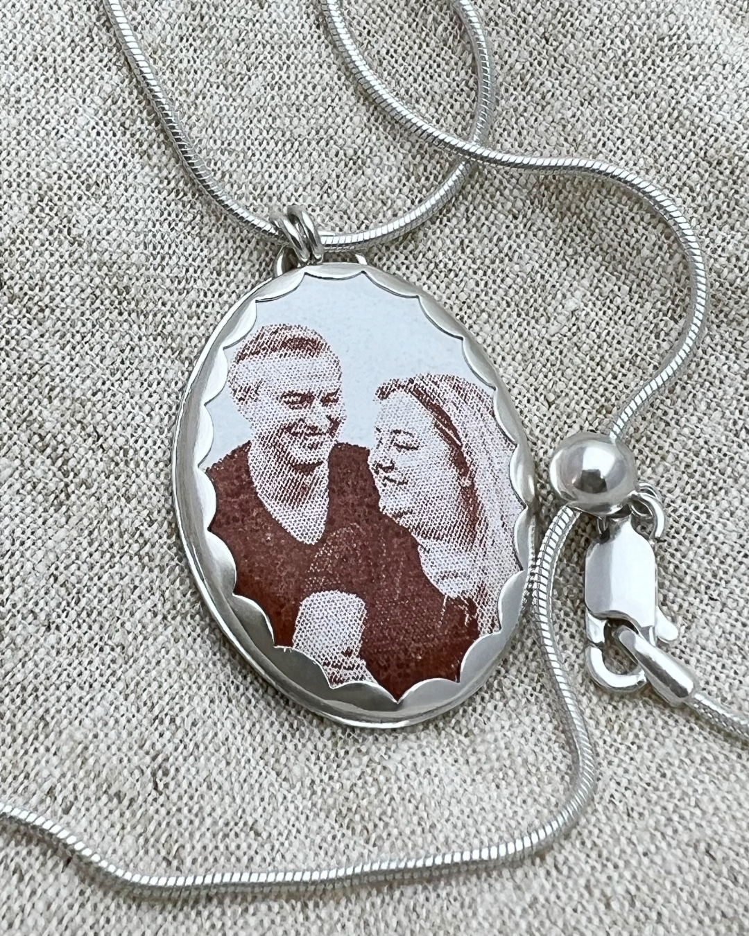 Silver necklace with a pendant featuring an enamel image of a couple on a textured beige background