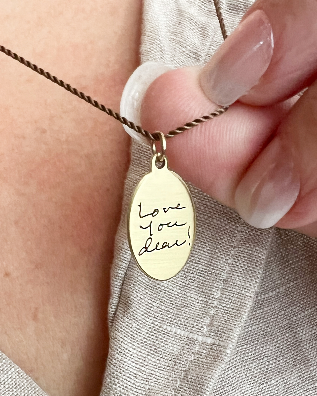 Gold necklace with 'Love You Dear' handwriting engraved - pendant held by a hand