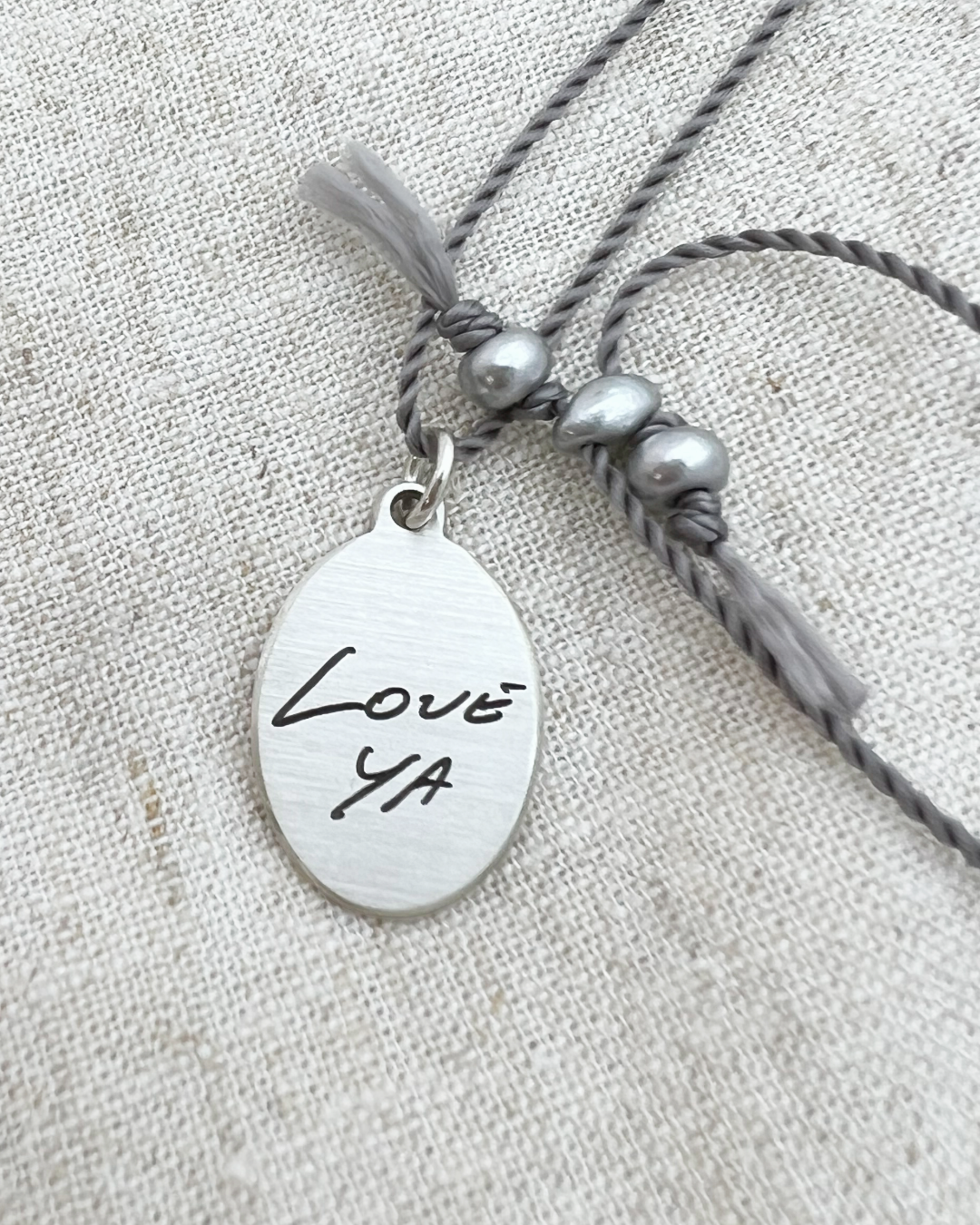Necklace with a pendant that says 'LOVE YA' engraved in handwriting on a textured fabric background