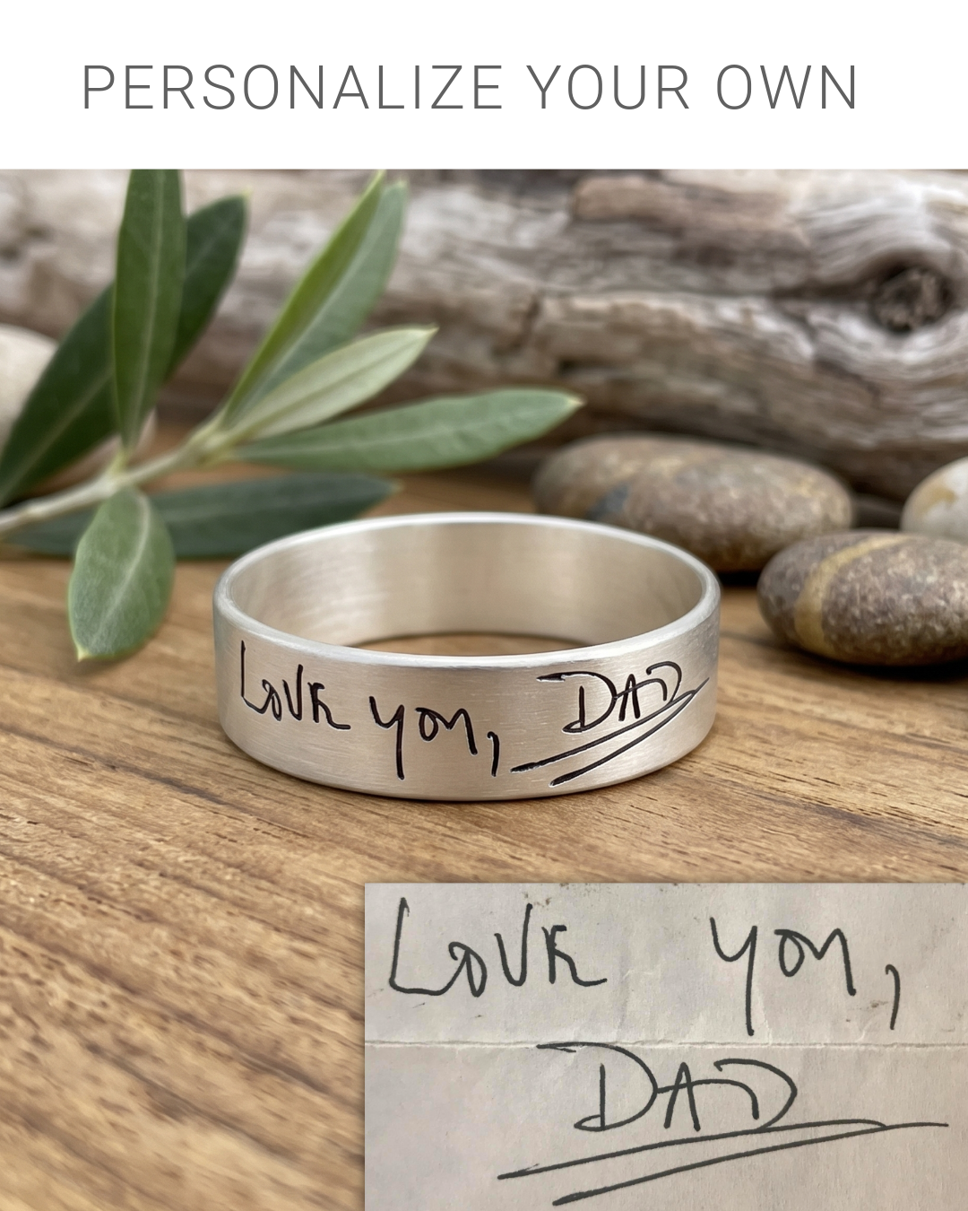 A silver engraved ring with the handwritten message 'Love you, Dad' resting on a wooden surface with decorative stones and olive leaves. A text banner at the top reads 'PERSONALIZE YOUR OWN' and a matching handwritten note graphic appears in the bottom right corner.