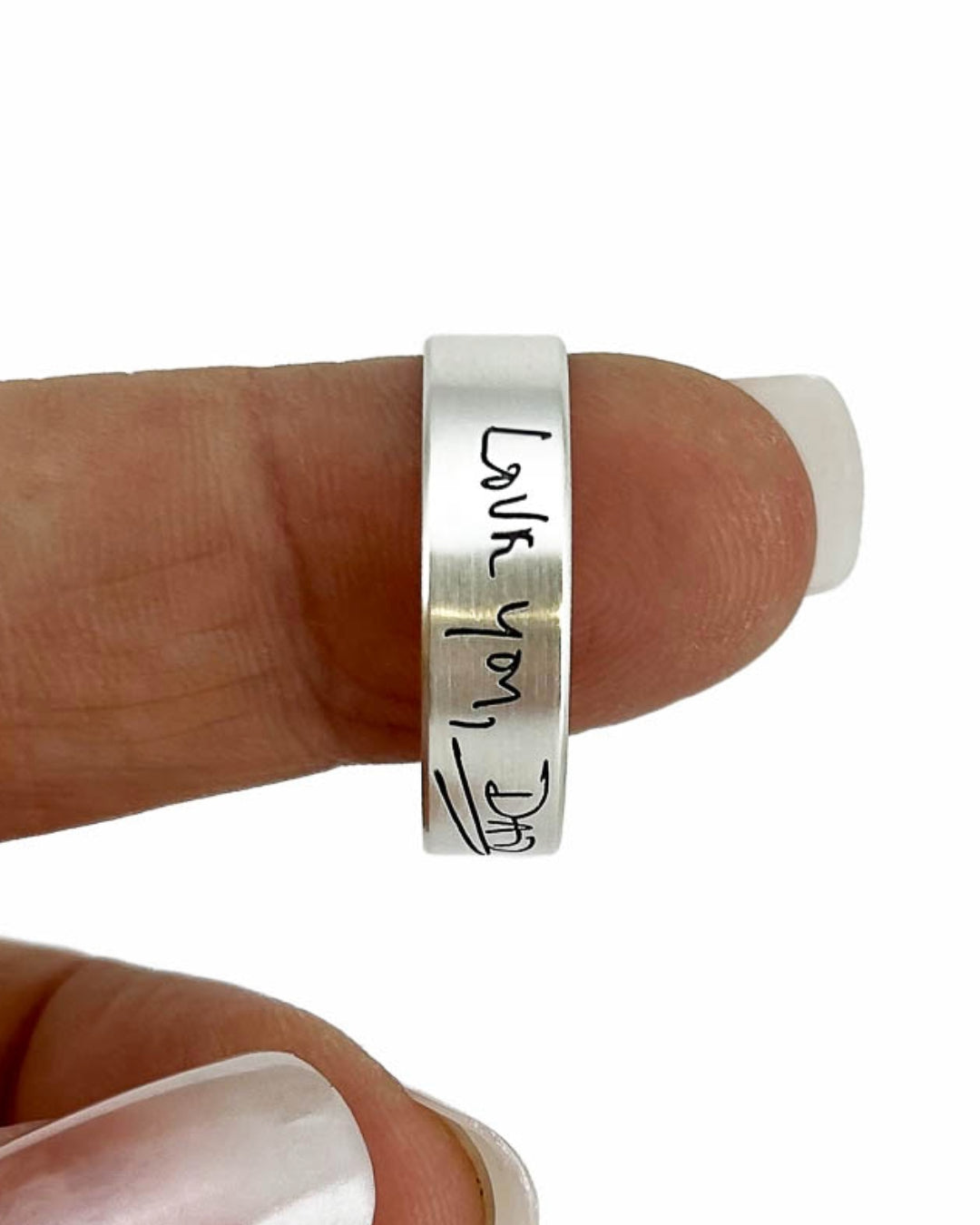 Silver ring with 'Love you, Dad' engraving on a finger against a white background