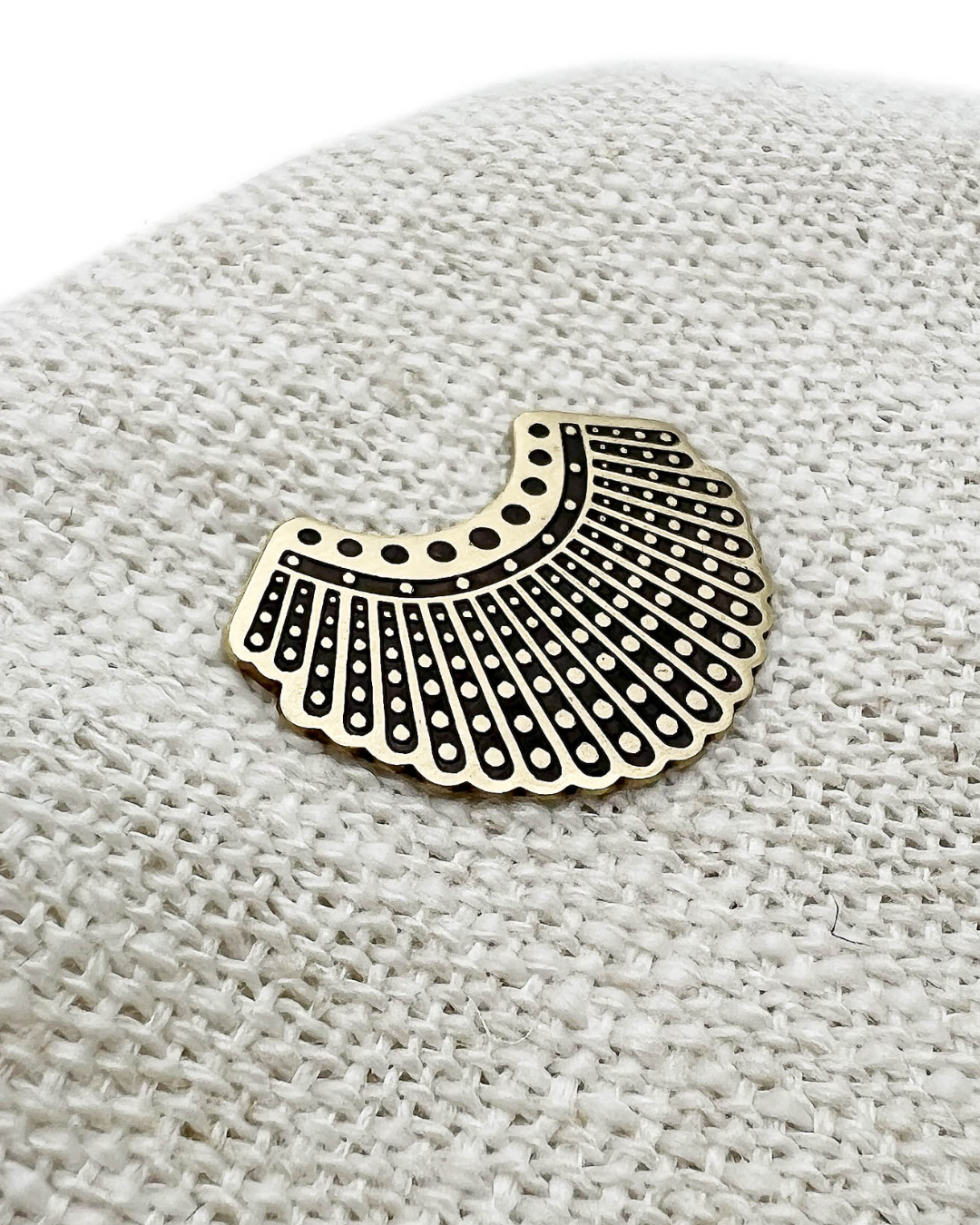 Decorative brass dissent collar brooch with black pattern on a textured beige surface