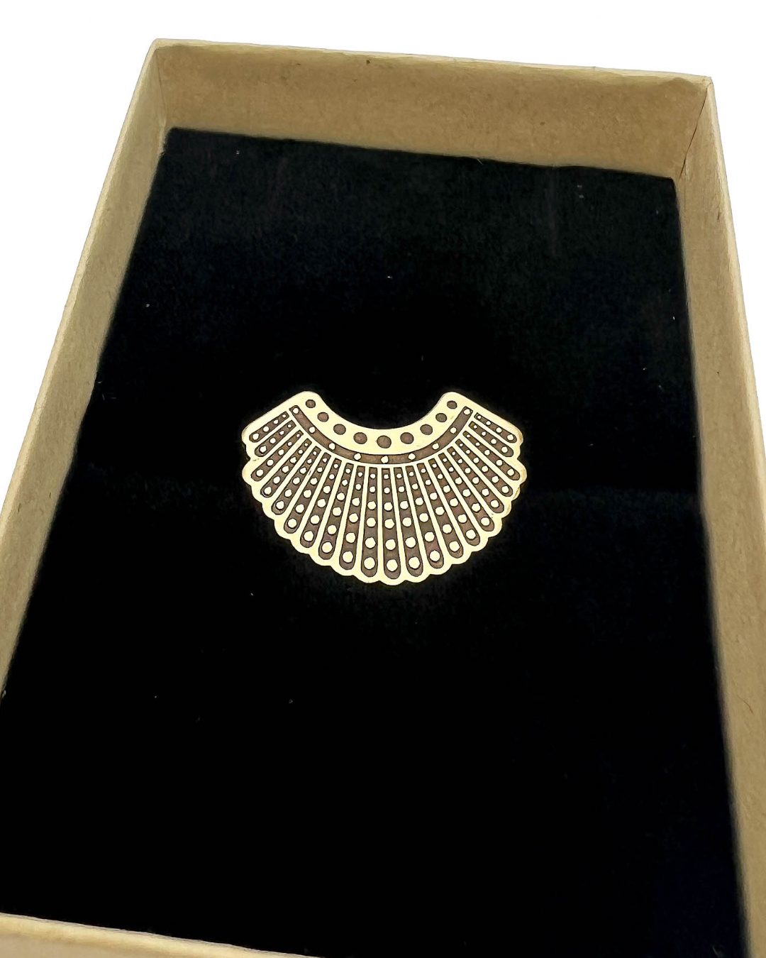 Brass dissent collar brooch on a black velvet cushion in a cardboard box