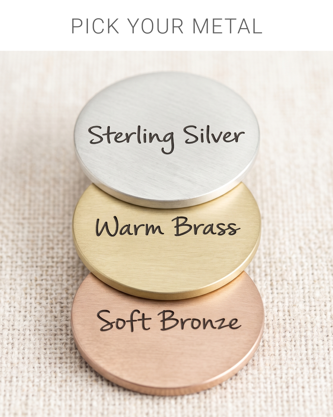 Three round metal discs stacked on a textured beige fabric background, labeled 'Sterling Silver,' 'Warm Brass,' and 'Soft Bronze,' with text at the top reading 'PICK YOUR METAL.'.