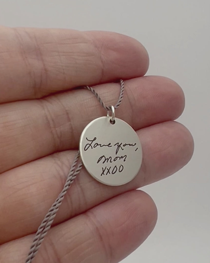 Small round personalized pendant engraved with handwriting and handprints. 