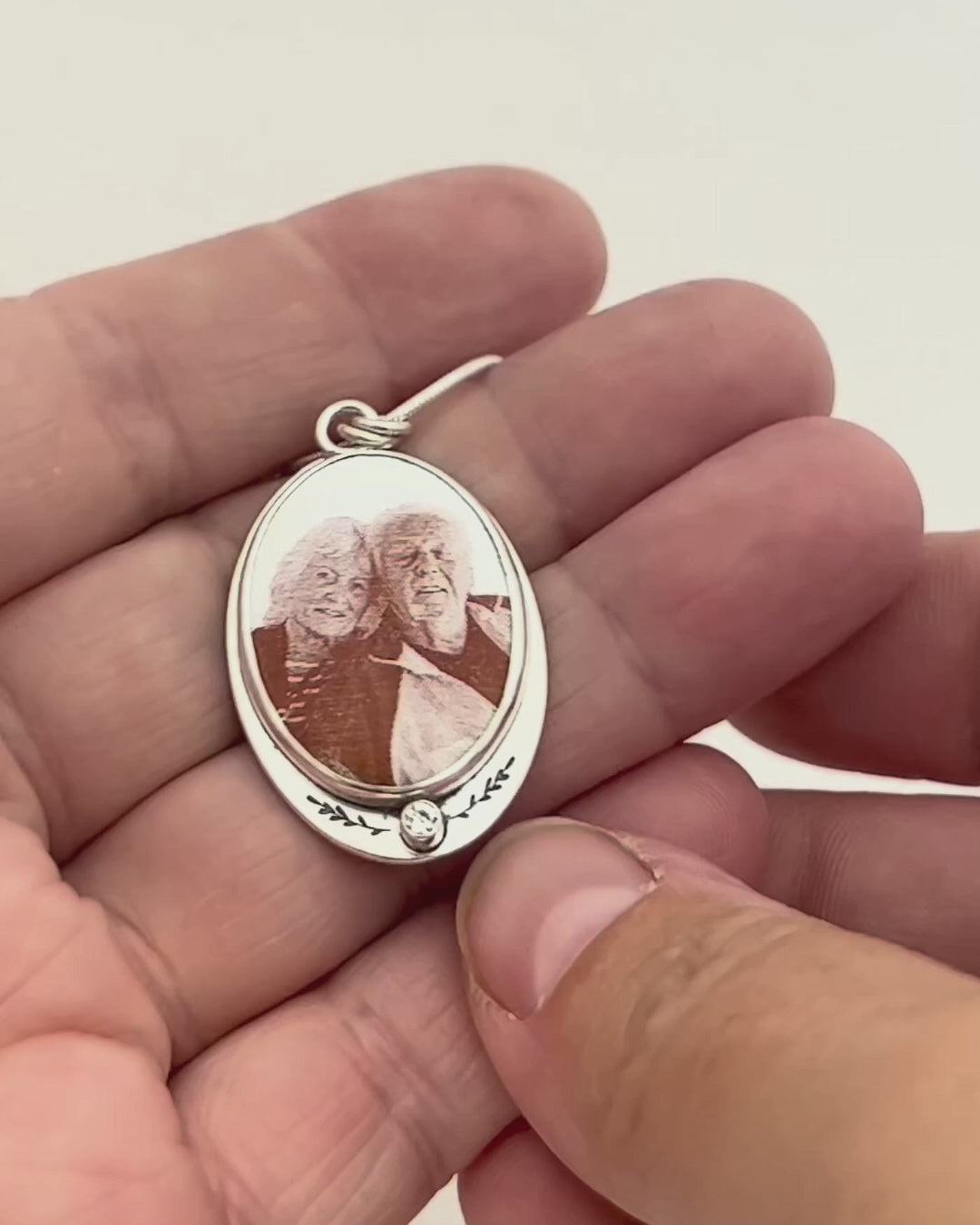Handcrafted silver memorial pendant with an enameled photograph on the front and a ring of flowers on the back with a raised butterfly detail. 