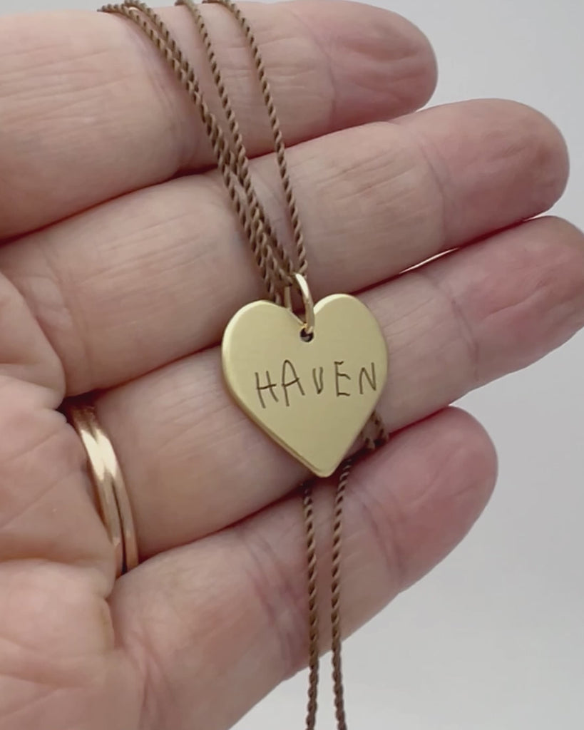 Personalized gold heart-shaped pendant with 'HAVEN' name engraved, held in a hand.