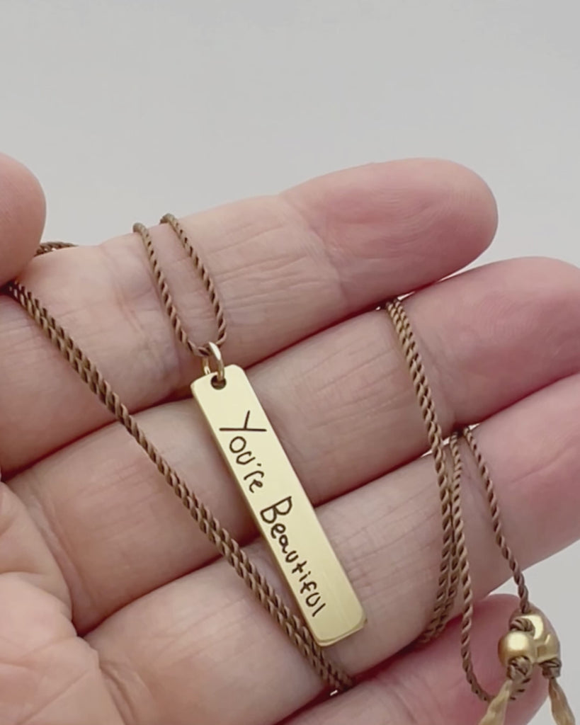 Kate handwriting pendant in brass moving in hand.
